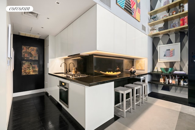 kitchen with dark countertops, modern cabinets, stainless steel oven, and white cabinets