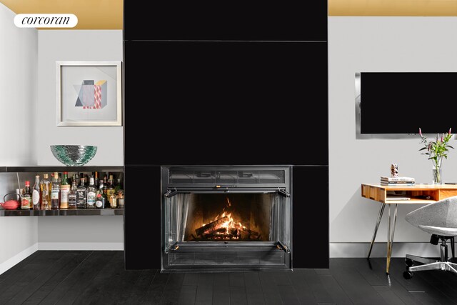 interior details with a bar, baseboards, wood finished floors, and a lit fireplace