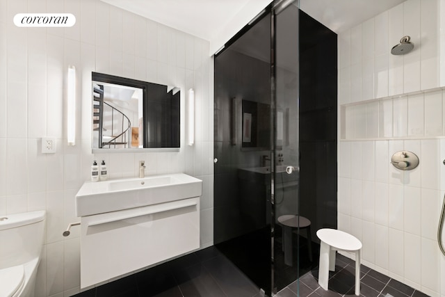 bathroom with tile walls, toilet, a stall shower, vanity, and tile patterned floors