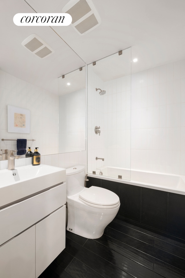 full bath featuring decorative backsplash, toilet, tiled shower / bath combo, vanity, and tile walls