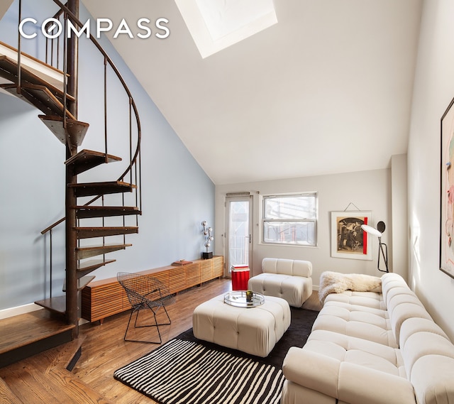 living area featuring a skylight, baseboards, wood finished floors, stairs, and high vaulted ceiling