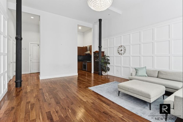 unfurnished living room with baseboards, wood-type flooring, an inviting chandelier, a high ceiling, and a decorative wall