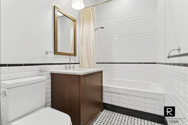 bathroom featuring toilet, a wainscoted wall, shower / tub combo, vanity, and tile walls