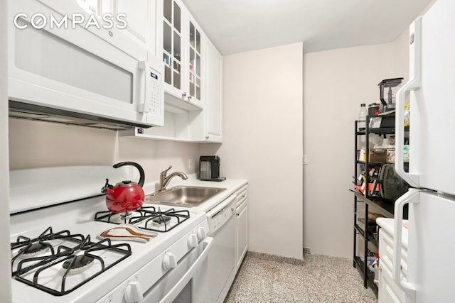 kitchen featuring white appliances, white cabinets, glass insert cabinets, light countertops, and a sink