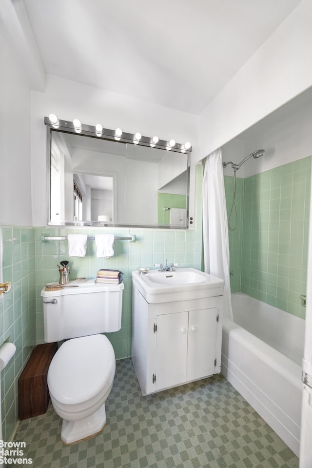 bathroom with tile walls, wainscoting, vanity, toilet, and shower / bath combo with shower curtain