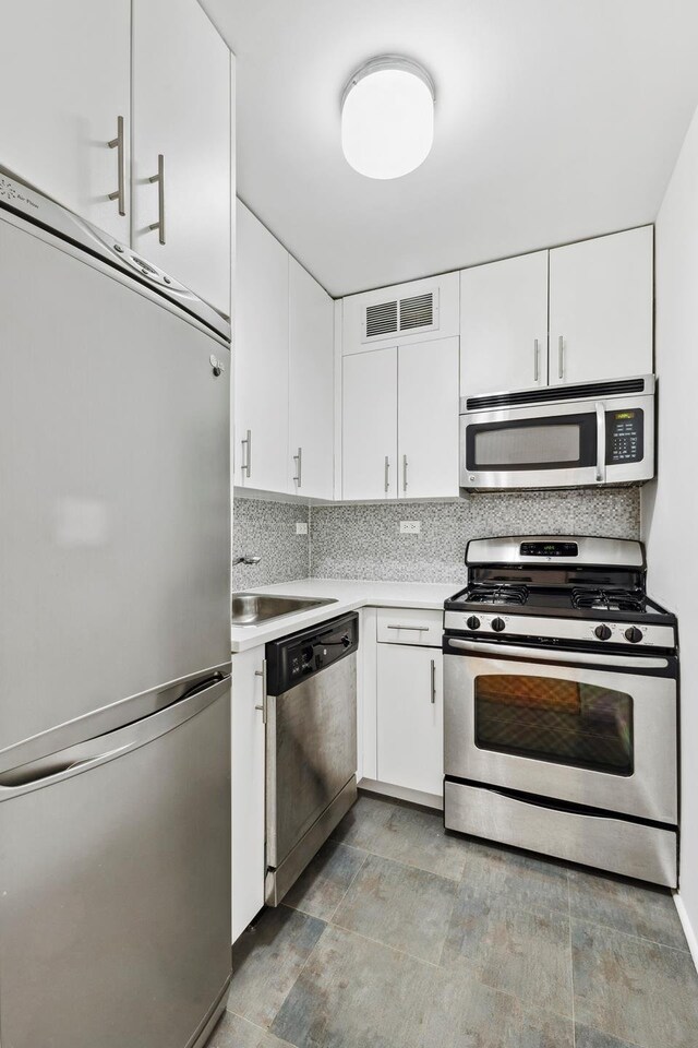 kitchen with visible vents, appliances with stainless steel finishes, a sink, light countertops, and backsplash