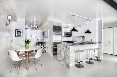 kitchen with concrete floors, decorative light fixtures, a kitchen bar, stone counters, and appliances with stainless steel finishes