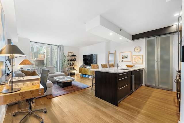 kitchen featuring light wood-style flooring, a peninsula, a sink, open floor plan, and light countertops