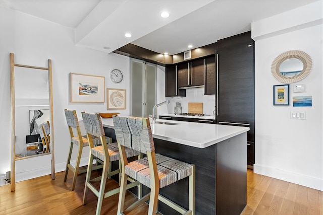 kitchen featuring a sink, baseboards, light wood-style floors, light countertops, and a kitchen breakfast bar