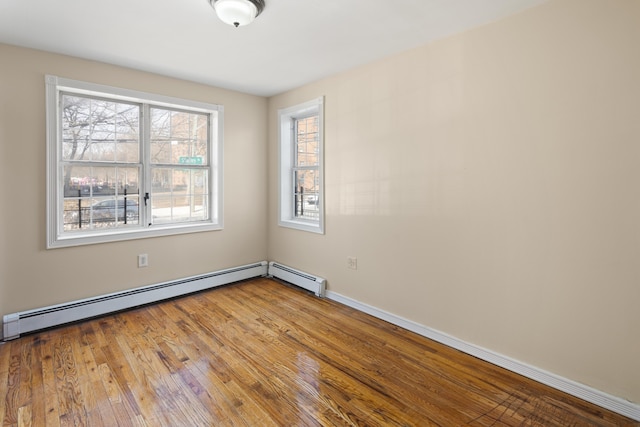 empty room with a baseboard heating unit, wood finished floors, and baseboards