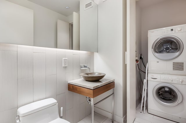 laundry room with stacked washing maching and dryer, visible vents, and a sink