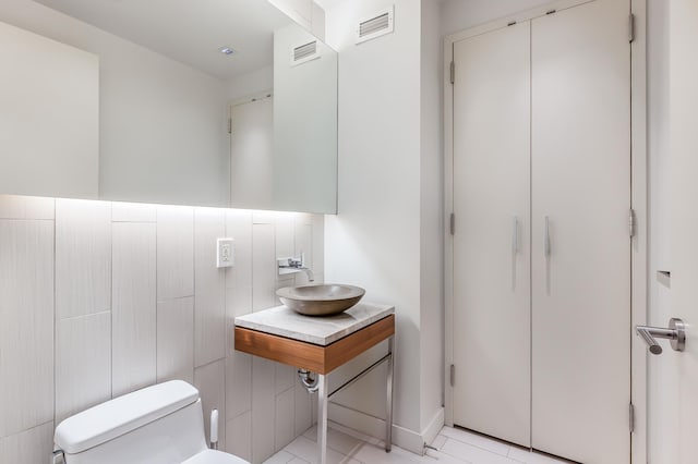 half bath with toilet, a sink, and visible vents