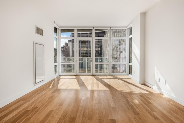 spare room featuring light wood finished floors, visible vents, floor to ceiling windows, and baseboards