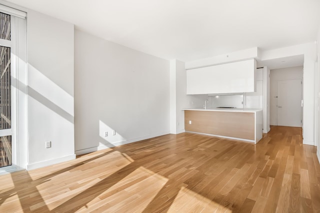 unfurnished living room with light wood-type flooring, a sink, and baseboards