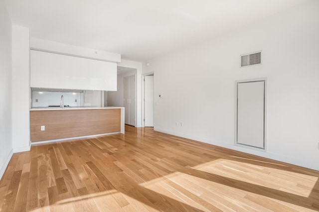 unfurnished living room featuring baseboards, visible vents, a sink, and light wood finished floors