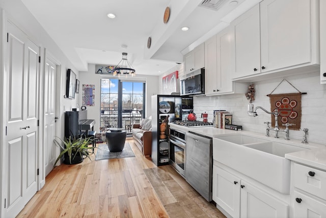 kitchen with a sink, stainless steel appliances, light countertops, tasteful backsplash, and a chandelier