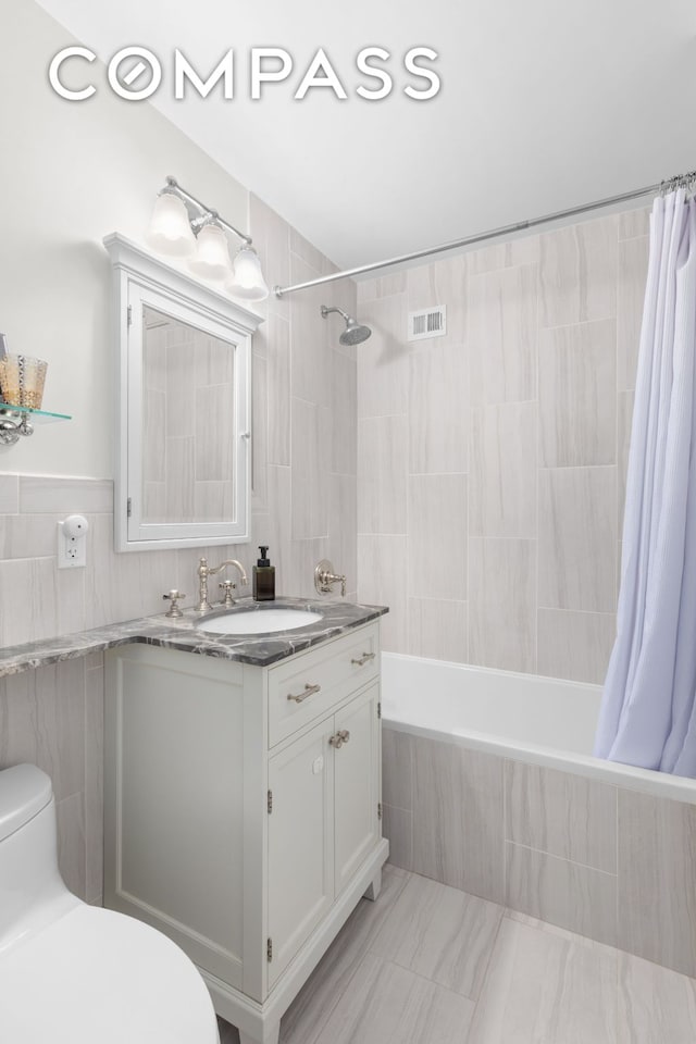 full bath featuring tile walls, tiled shower / bath, visible vents, toilet, and vanity