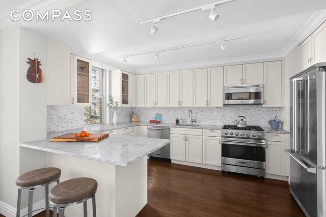 kitchen featuring white cabinets, premium appliances, glass insert cabinets, a kitchen breakfast bar, and a peninsula