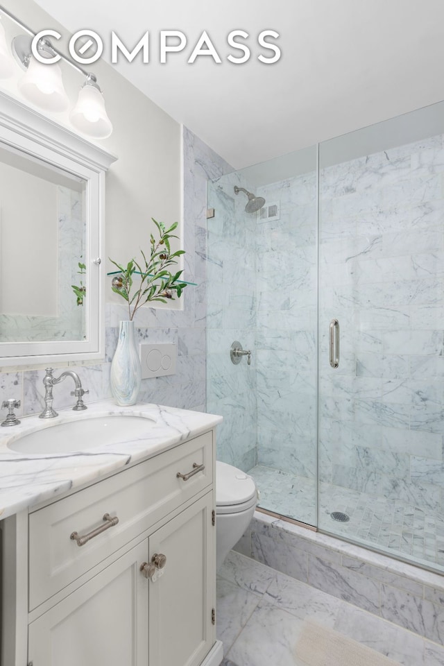 bathroom with marble finish floor, vanity, a marble finish shower, and toilet