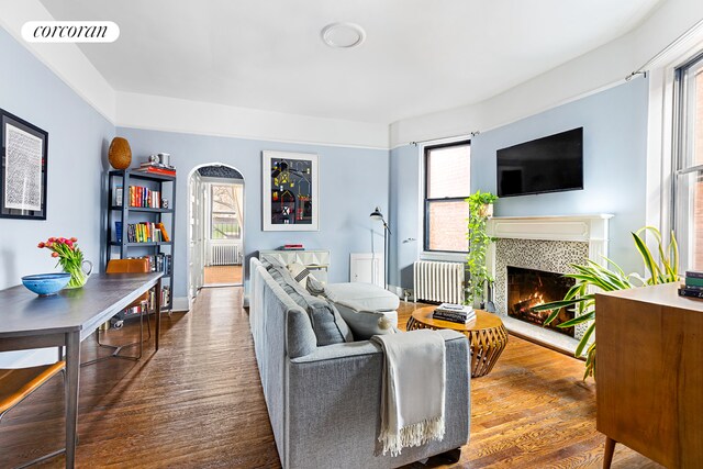 living area with visible vents, a tiled fireplace, radiator heating unit, a healthy amount of sunlight, and wood finished floors