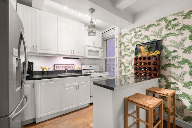 kitchen featuring white appliances, a sink, white cabinetry, light wood finished floors, and wallpapered walls