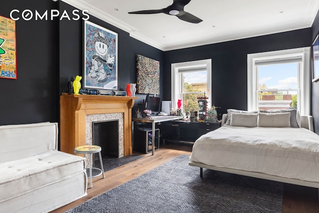 bedroom featuring ornamental molding, a fireplace, wood finished floors, and a ceiling fan