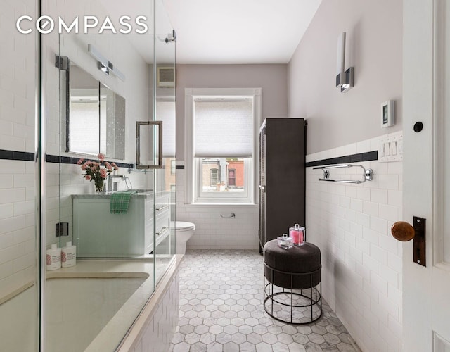 bathroom featuring tile patterned flooring, a tile shower, tile walls, and toilet