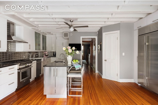 kitchen with dark countertops, wall chimney range hood, glass insert cabinets, and premium appliances