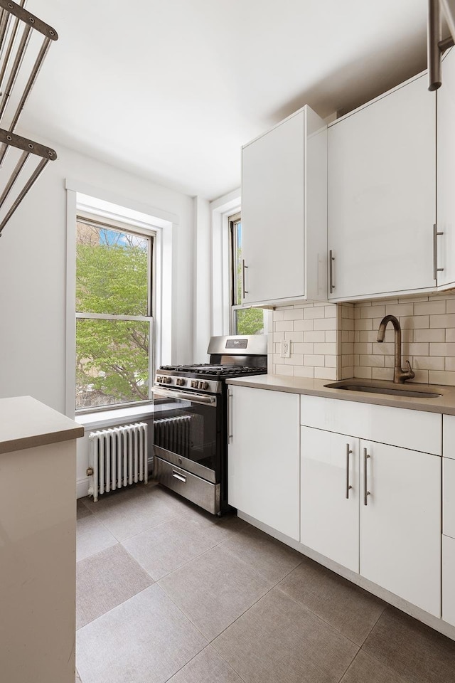 kitchen with a sink, decorative backsplash, stainless steel range with gas stovetop, and radiator heating unit