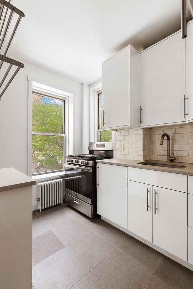 626 E 14th St Unit 11/12, New York City, NY 10009 - kitchen featuring radiator heating unit, stainless steel gas range oven, a sink, decorative backsplash, and white cabinets