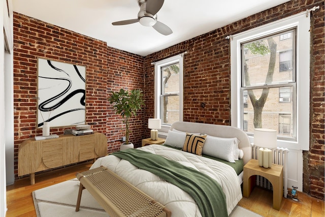 bedroom featuring brick wall, light wood-style flooring, and radiator