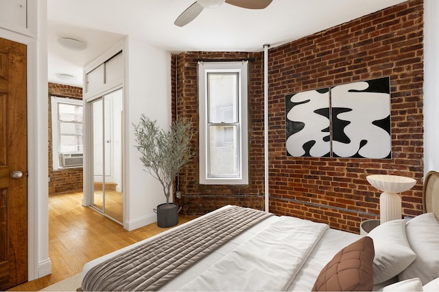 bedroom with a closet, ceiling fan, brick wall, light wood-type flooring, and baseboards