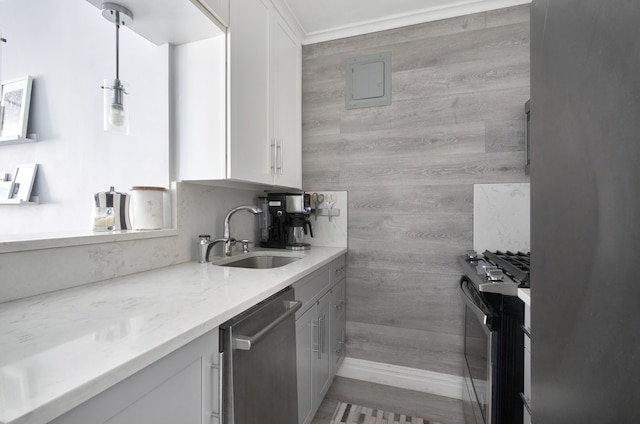 kitchen with a sink, stainless steel appliances, white cabinetry, light stone counters, and wood walls