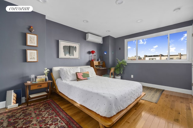 bedroom with a wall mounted air conditioner, wood-type flooring, visible vents, and baseboards