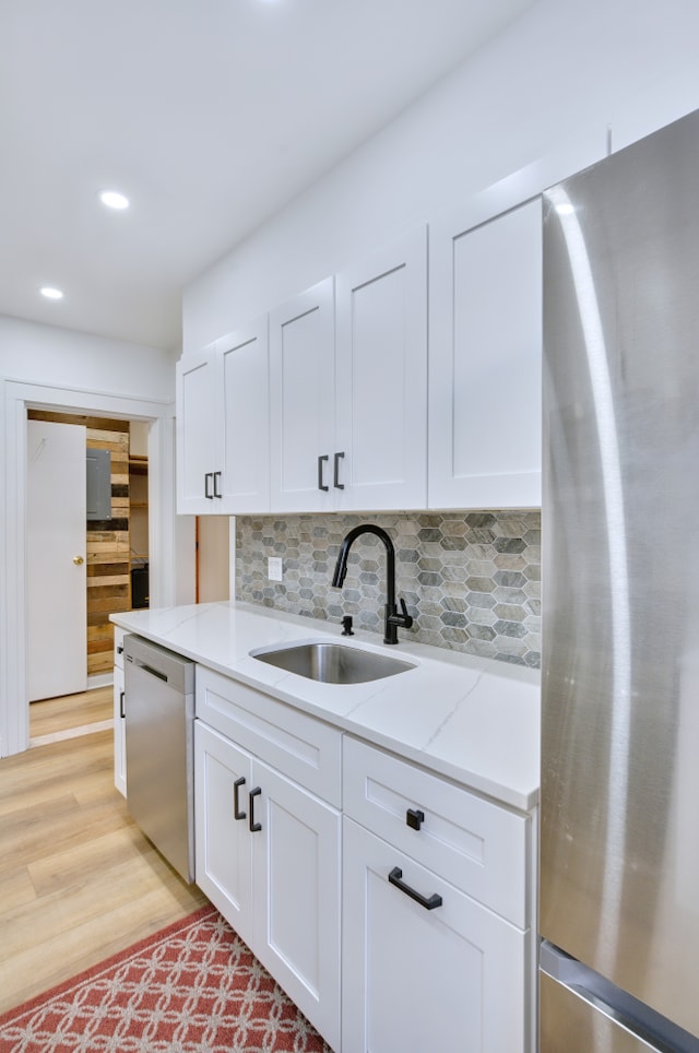 kitchen with light stone counters, stainless steel appliances, a sink, light wood finished floors, and tasteful backsplash