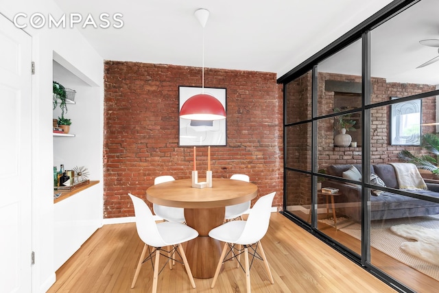 dining area featuring brick wall, light wood-type flooring, and baseboards