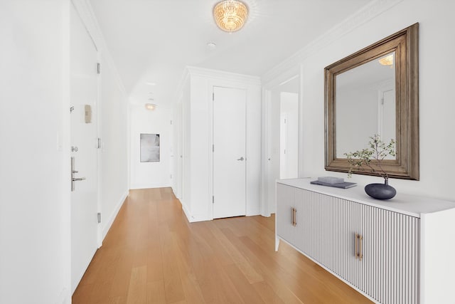 hall featuring baseboards, crown molding, and light wood-style floors