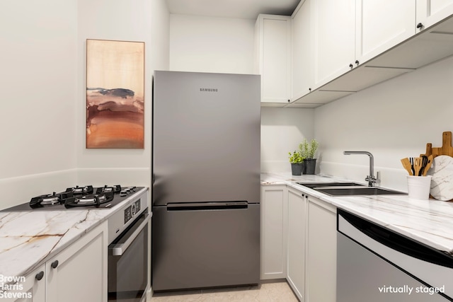 kitchen with a sink, light stone counters, appliances with stainless steel finishes, and white cabinets