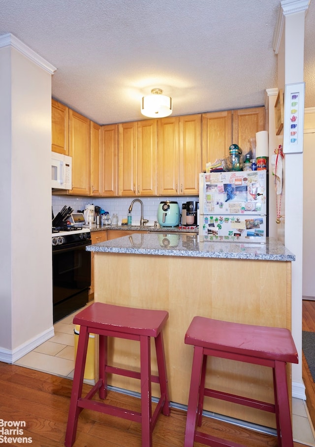 kitchen featuring light stone counters, a breakfast bar area, white appliances, light wood finished floors, and tasteful backsplash