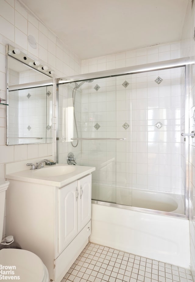 bathroom with tile walls, combined bath / shower with glass door, vanity, and toilet