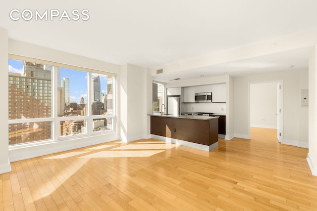 unfurnished living room with light wood-style floors, a city view, a sink, and baseboards