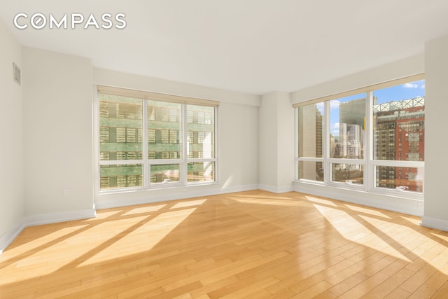 spare room with a wealth of natural light, baseboards, visible vents, and wood finished floors