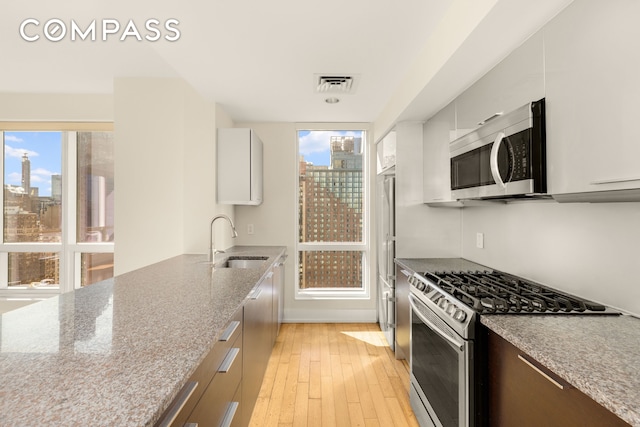 kitchen featuring visible vents, appliances with stainless steel finishes, a view of city, light wood-type flooring, and a sink