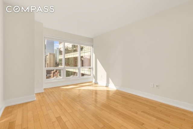 empty room featuring light wood-type flooring, a view of city, and baseboards