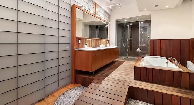 bathroom with a shower stall, wood finished floors, vanity, a bath, and wainscoting