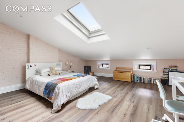 bedroom with vaulted ceiling with skylight, brick wall, baseboards, and wood finished floors