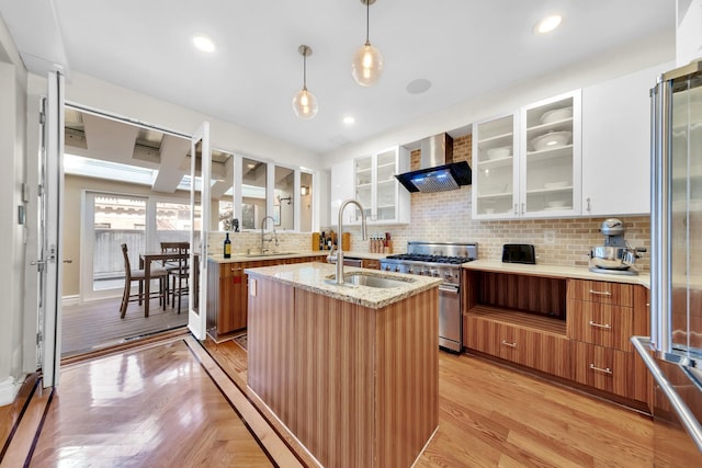 kitchen with backsplash, brown cabinetry, a sink, high quality appliances, and wall chimney exhaust hood