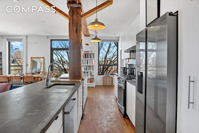 kitchen featuring white cabinets, wood-type flooring, appliances with stainless steel finishes, pendant lighting, and a sink