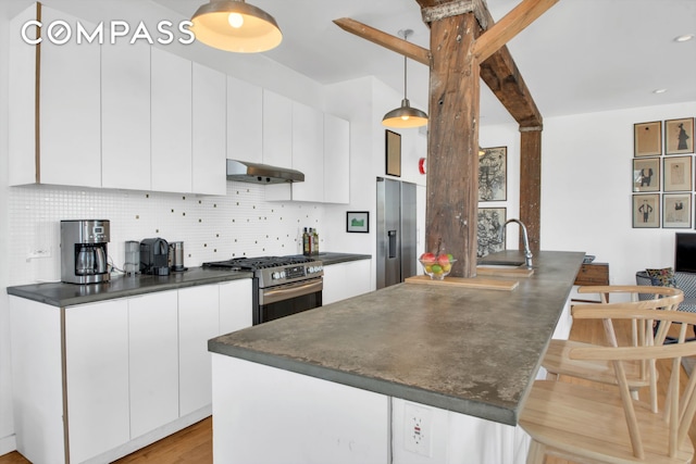 kitchen featuring tasteful backsplash, dark countertops, appliances with stainless steel finishes, a peninsula, and under cabinet range hood