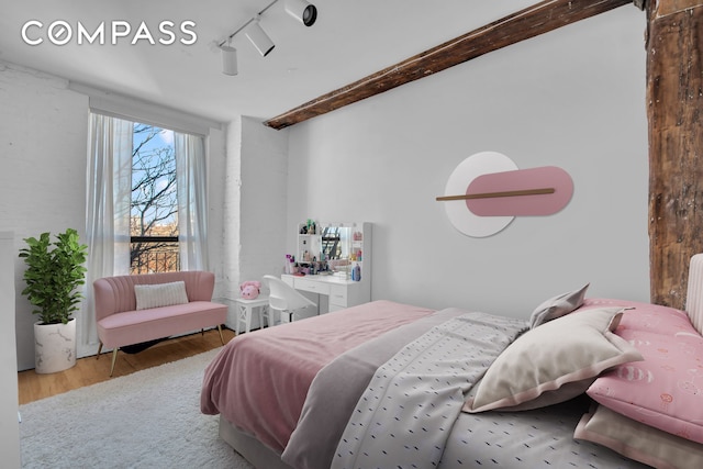 bedroom with rail lighting, beam ceiling, and wood finished floors